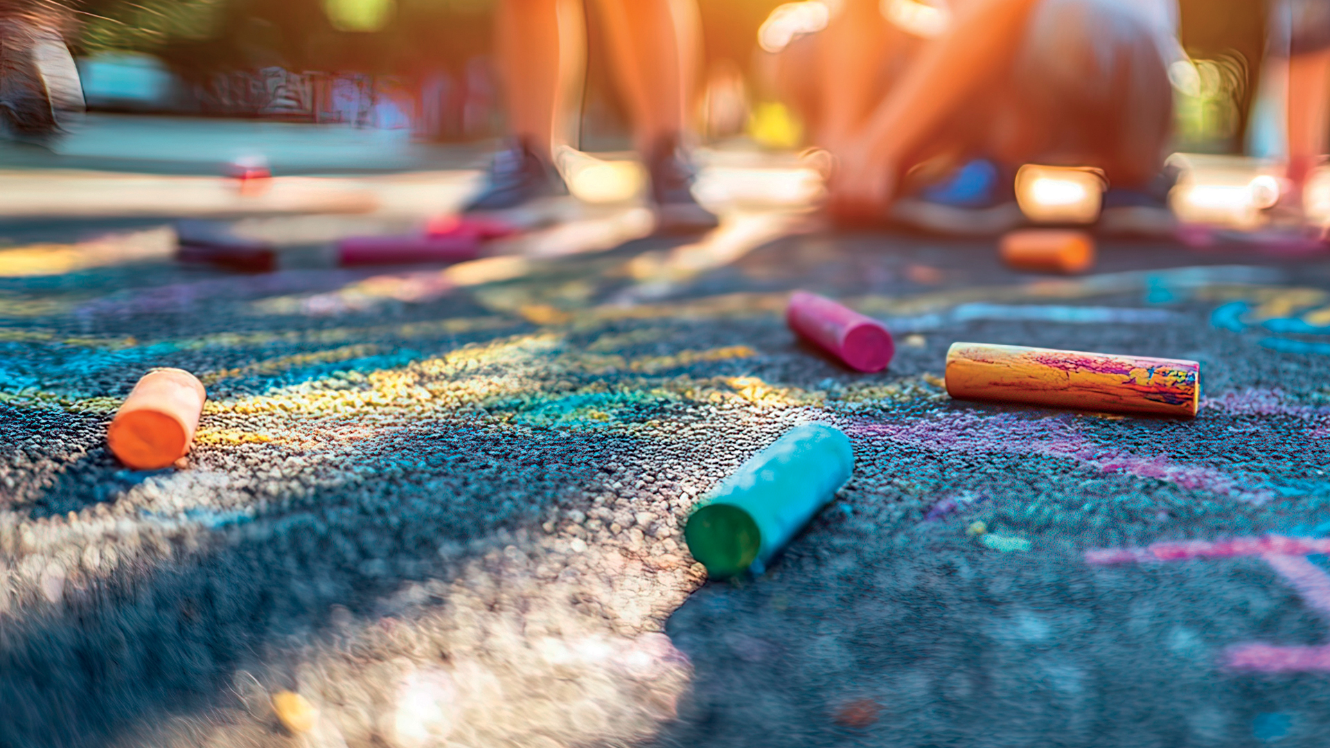 Children drawing colorful chalk art on asphalt pavement outdoors during summer.