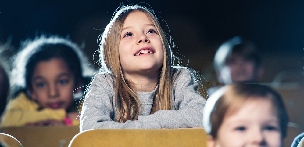 Selective focus of cute smiling child watching movie together with multicultural friends