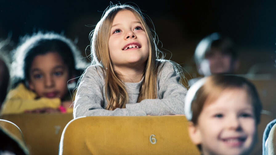 Selective focus of cute smiling child watching movie together with multicultural friends