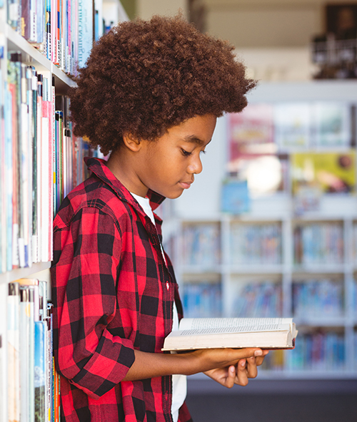 Happy african american schoolboy reading book standing in school