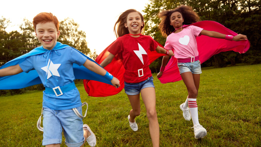 Carefree diverse superhero children running along meadow