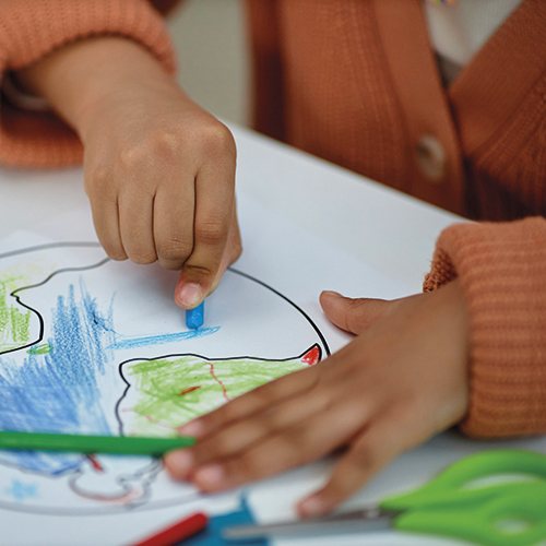 Close up of unrecognizable little girl coloring planet earth in preschool